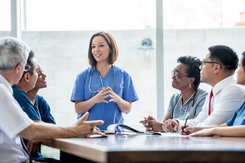 A female medical professional talks with a group of medical professional